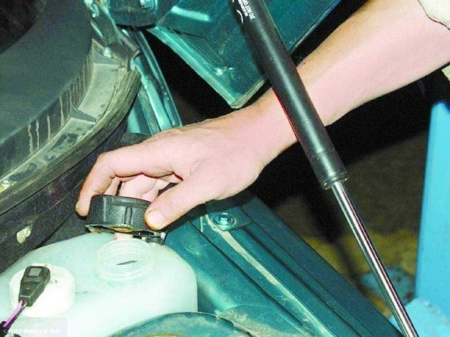 Расширительный бачок охлаждающей жидкости в автомобиле ВАЗ-2110 и крышка в руке